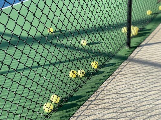 pickleballs lined up along bottom of pickleball court fence