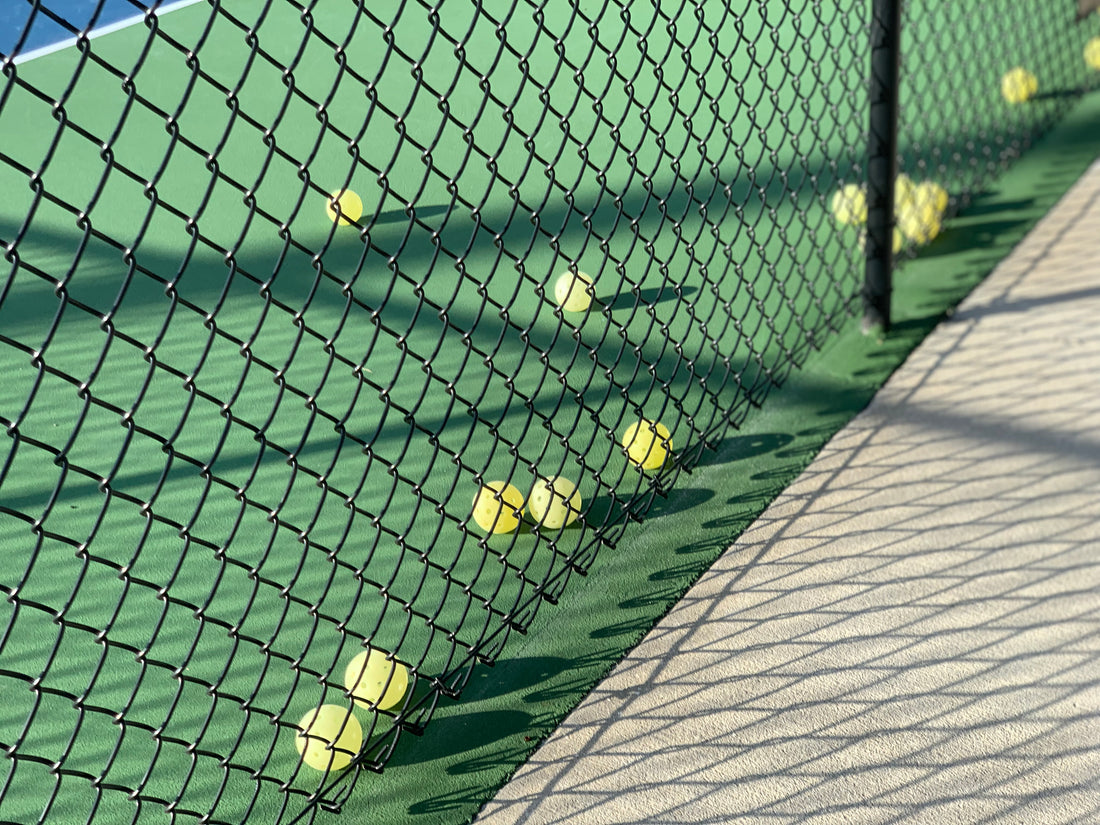 pickleballs lined up along bottom of pickleball court fence 